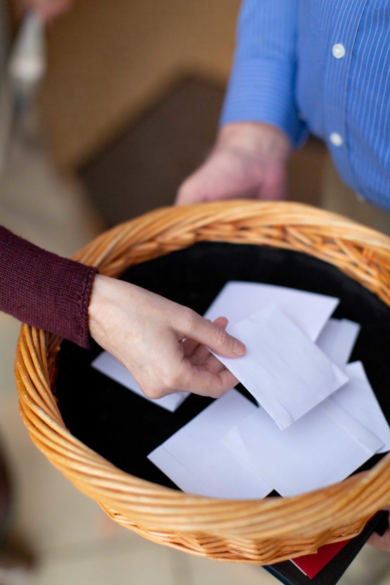 A hand places an offering envelope in a basket